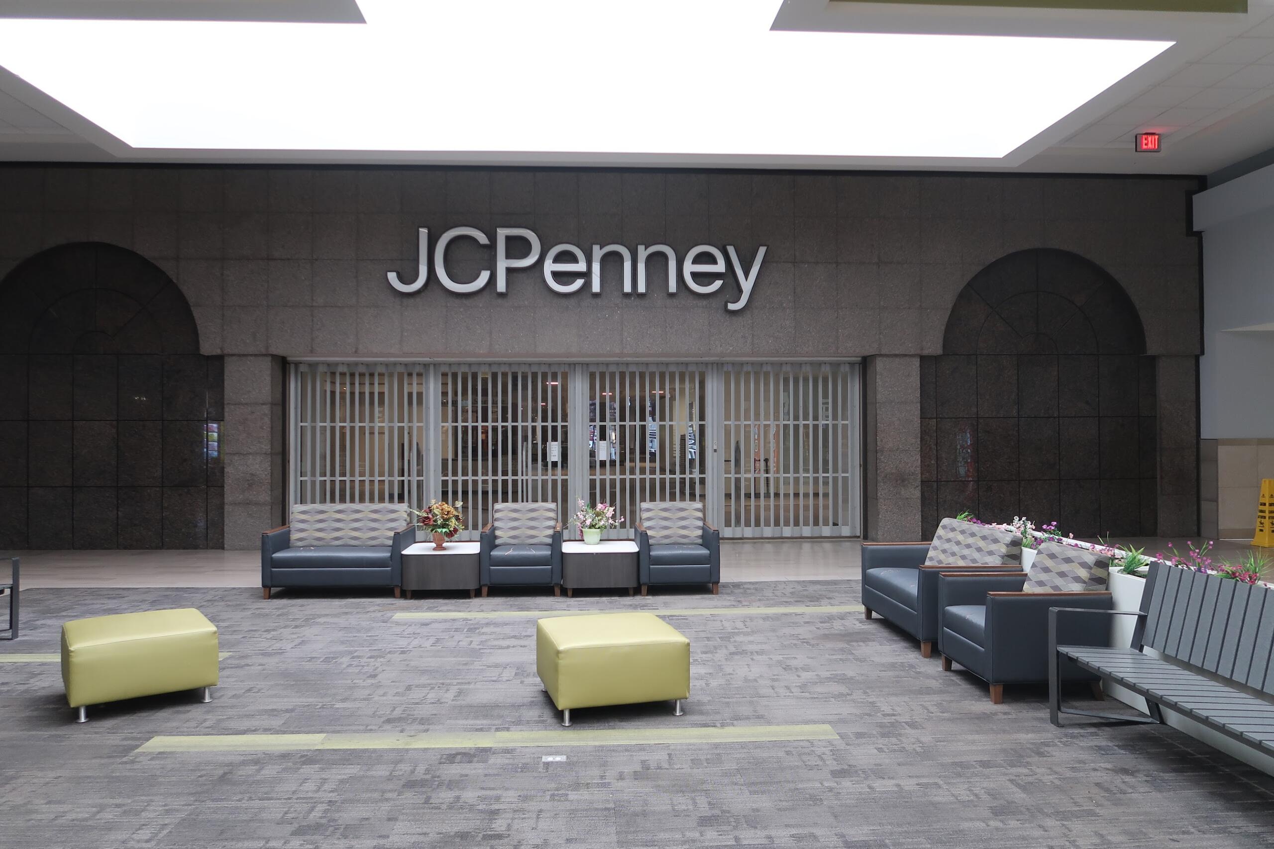 Seating lounge in a mall in front of a JC Penney storefront with gray couches and small tables with flowers.
