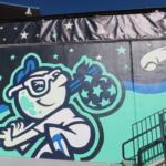 Cartoon astronaut floating among stars on a mural, with teal and blue waves and a metal railing in the foreground.