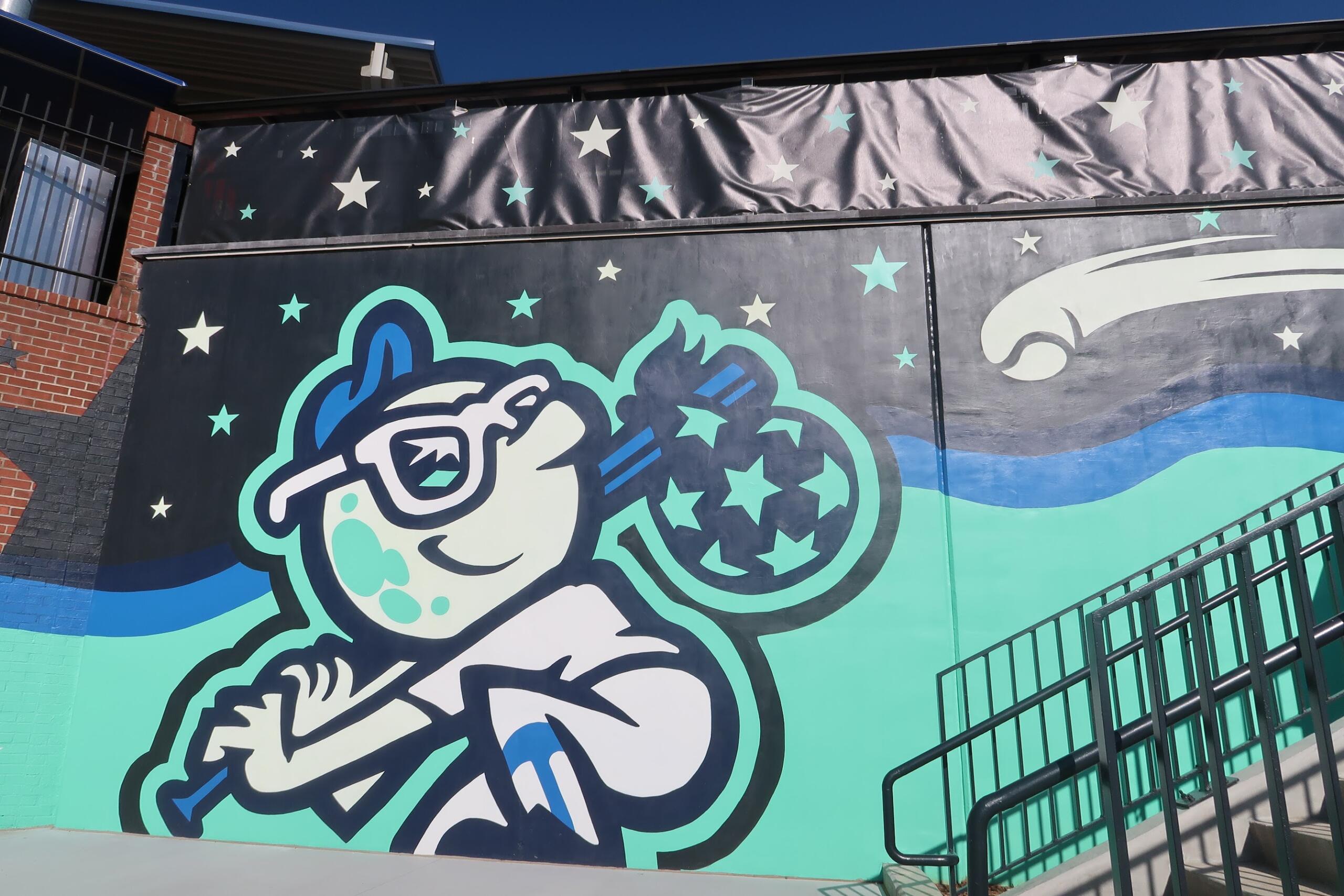 Cartoon astronaut floating among stars on a mural, with teal and blue waves and a metal railing in the foreground.