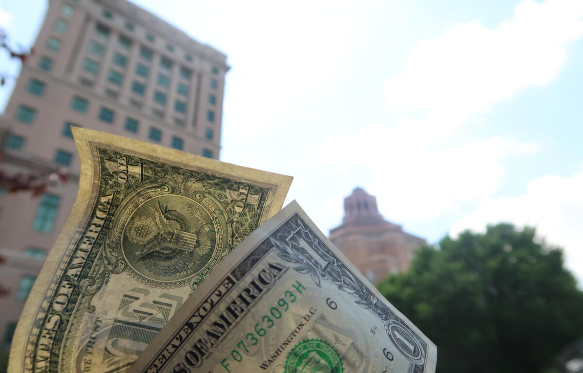 Close-up of overlapping US dollar bills held in front of a blurred cityscape background.