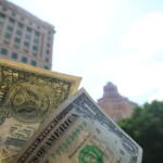 Close-up of overlapping US dollar bills held in front of a blurred cityscape background.