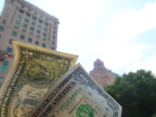 Close-up of overlapping US dollar bills held in front of a blurred cityscape background.