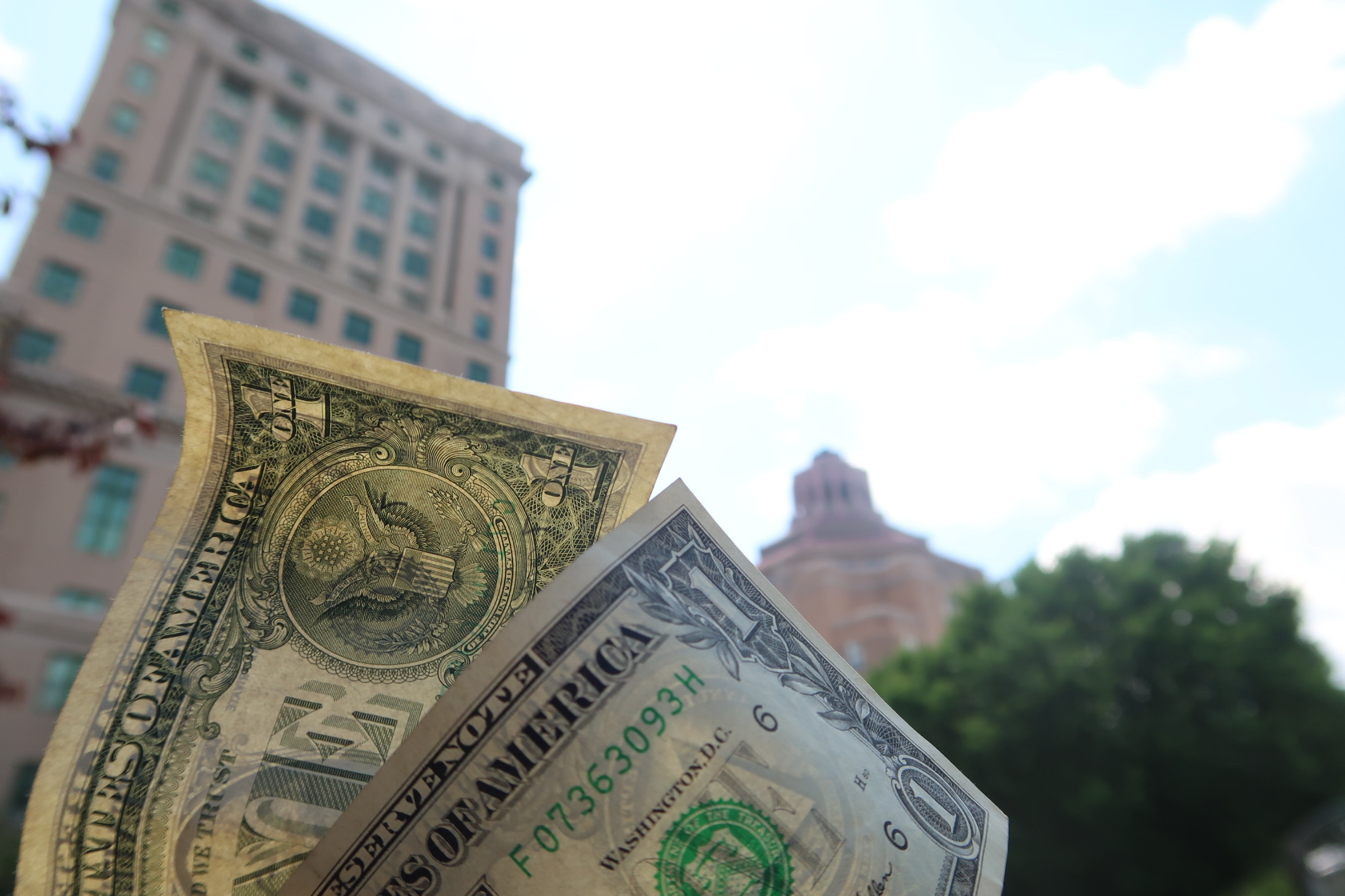 Close-up of overlapping US dollar bills held in front of a blurred cityscape background.