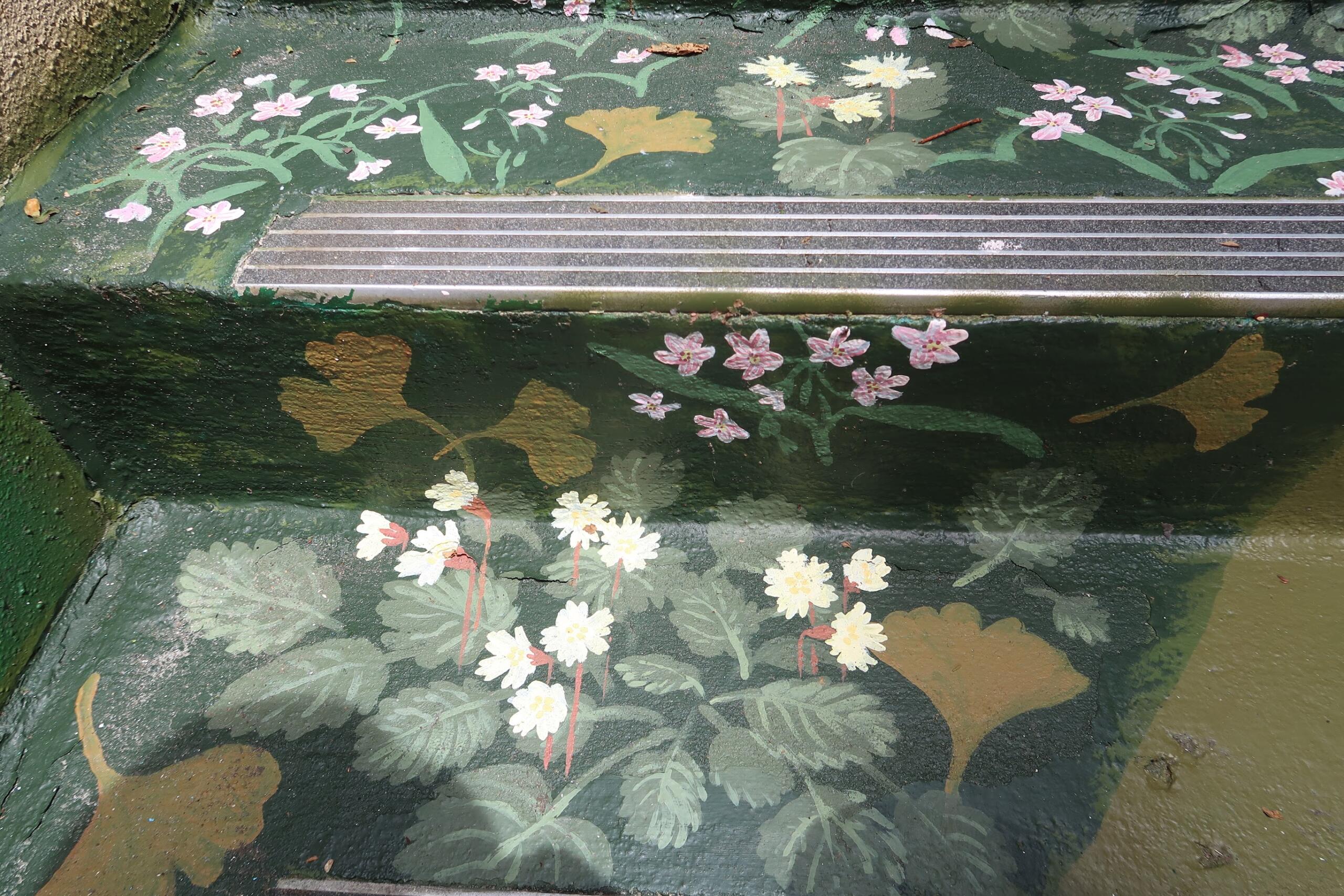 Painted floral mural on a stair riser with pink and white flowers and green leaves, across a metal strip.