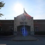 Front of Asheville Fire & Rescue station with an American flag on a flagpole and a bright sun flare over the roof
