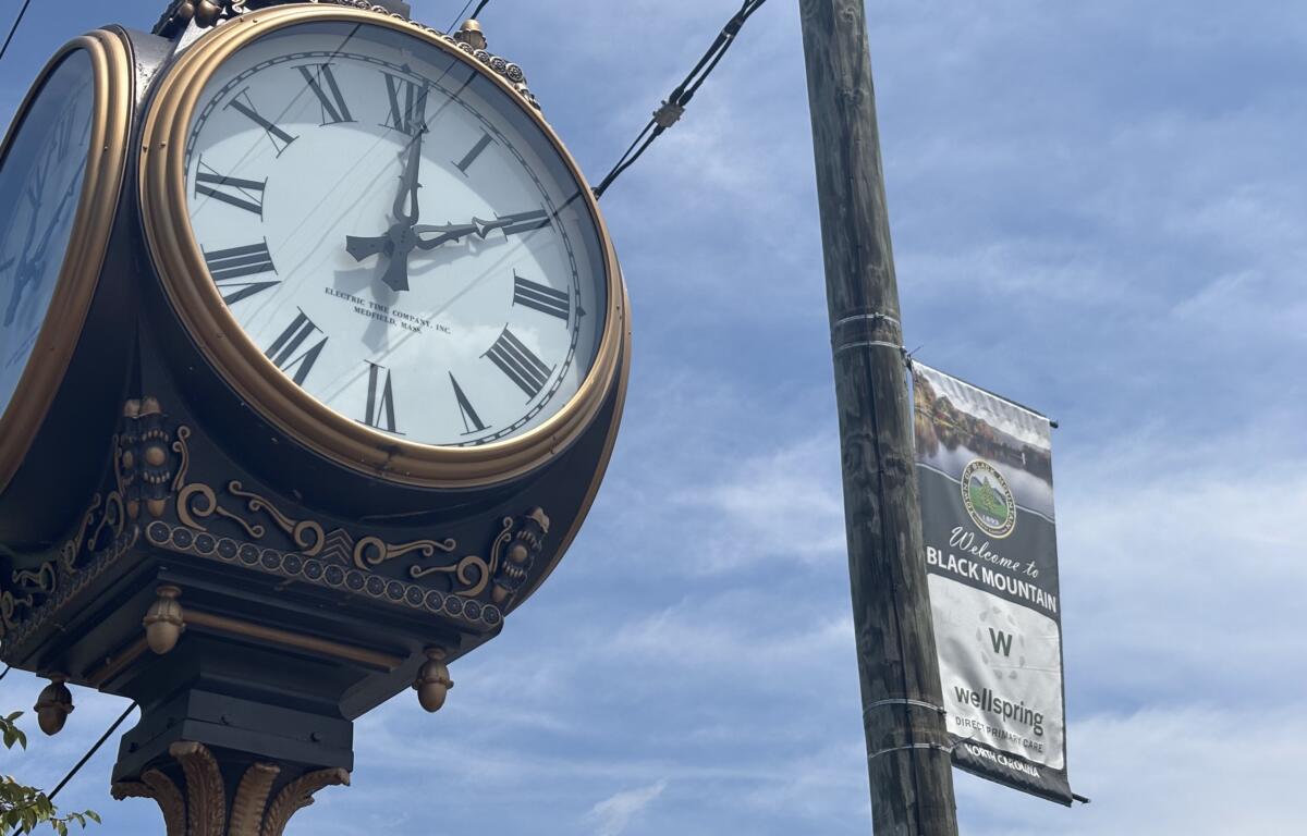 Ornate vintage clock with Roman numerals and gold trim mounted on a decorative post against a blue sky.
