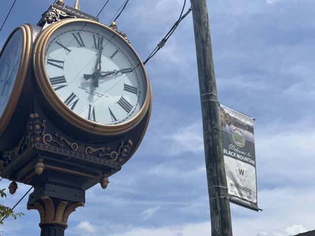 Ornate vintage clock with Roman numerals and gold trim mounted on a decorative post against a blue sky.