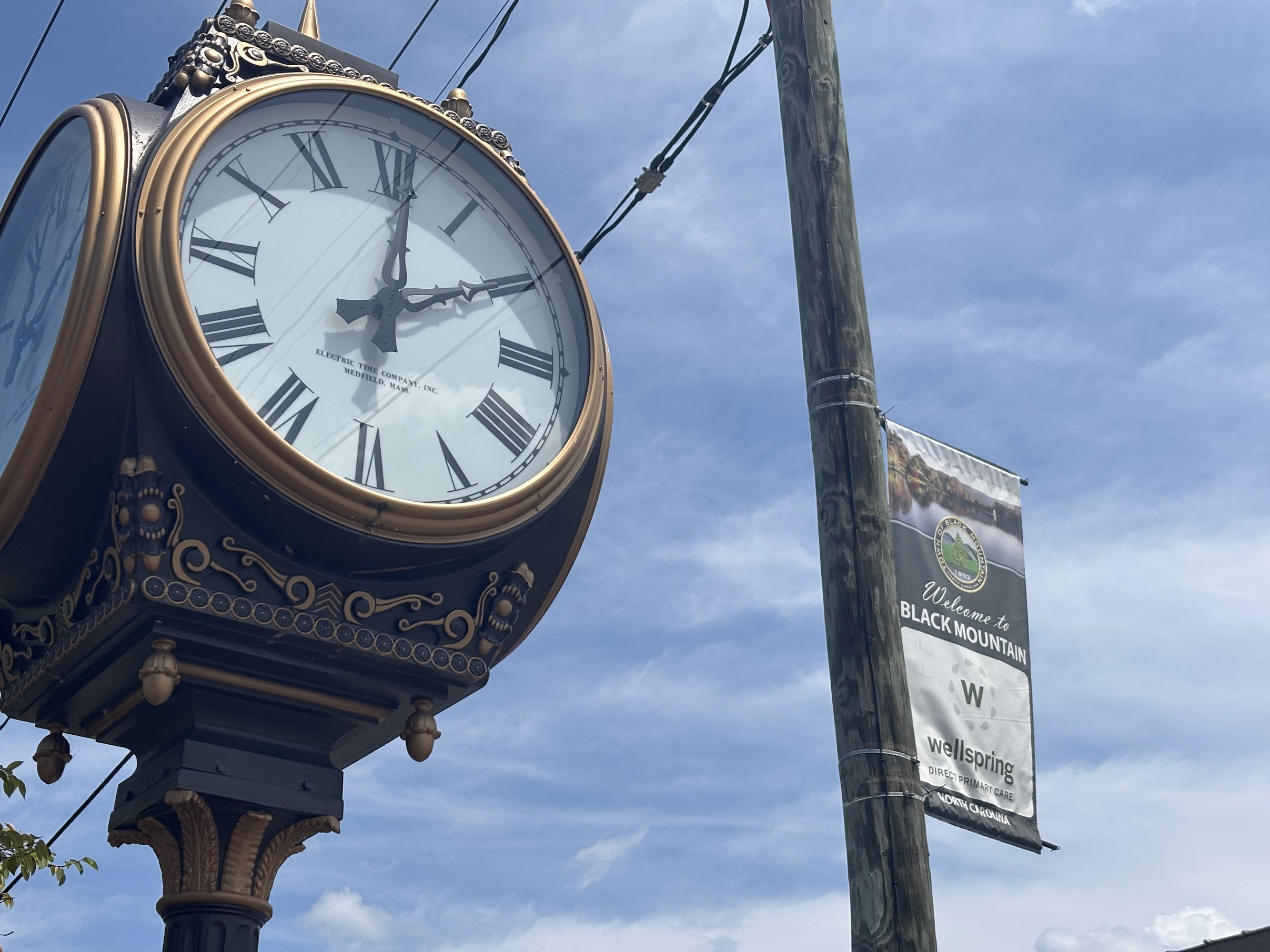 Ornate vintage clock with Roman numerals and gold trim mounted on a decorative post against a blue sky.