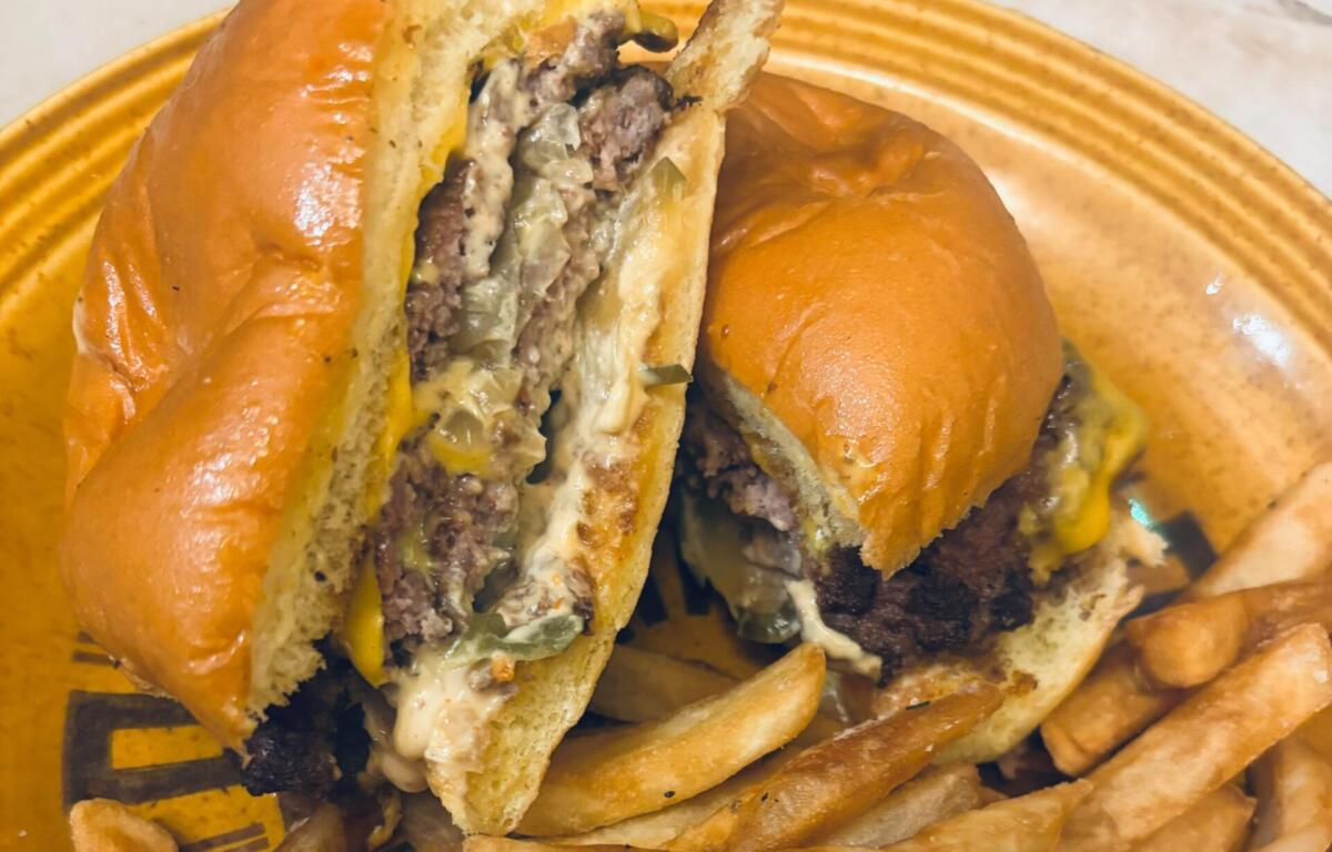 Two halves of a cheeseburger with melted cheese and onions on a toasted bun, with French fries on a yellow plate.