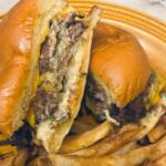 Two halves of a cheeseburger with melted cheese and onions on a toasted bun, with French fries on a yellow plate.