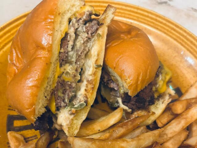 Two halves of a cheeseburger with melted cheese and onions on a toasted bun, with French fries on a yellow plate.