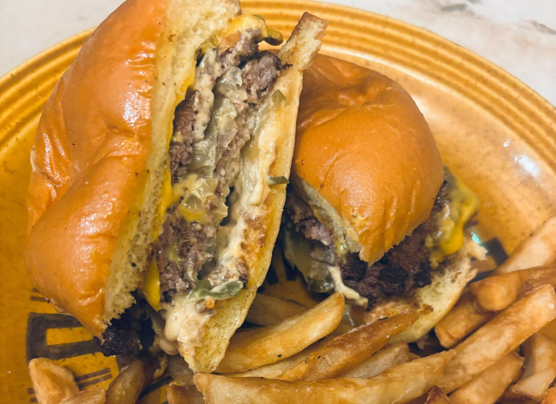 Two halves of a cheeseburger with melted cheese and onions on a toasted bun, with French fries on a yellow plate.