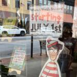Storefront window with a large 'Starting July 1st' sign and colorful kids' posters visible through the glass.