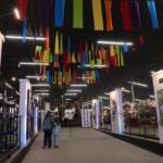 Indoor exhibition hall with booths and multicolored fabric ribbons hanging from the ceiling overhead.