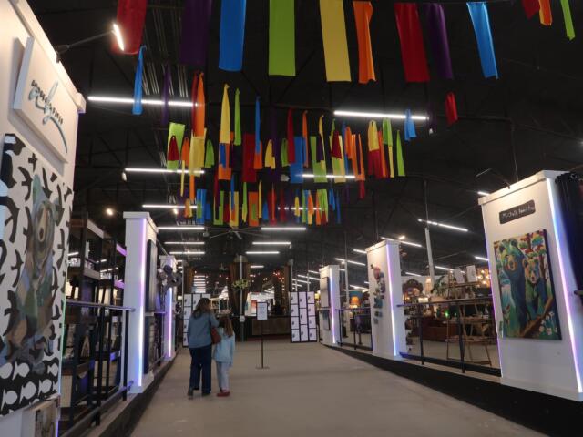 Indoor exhibition hall with booths and multicolored fabric ribbons hanging from the ceiling overhead.