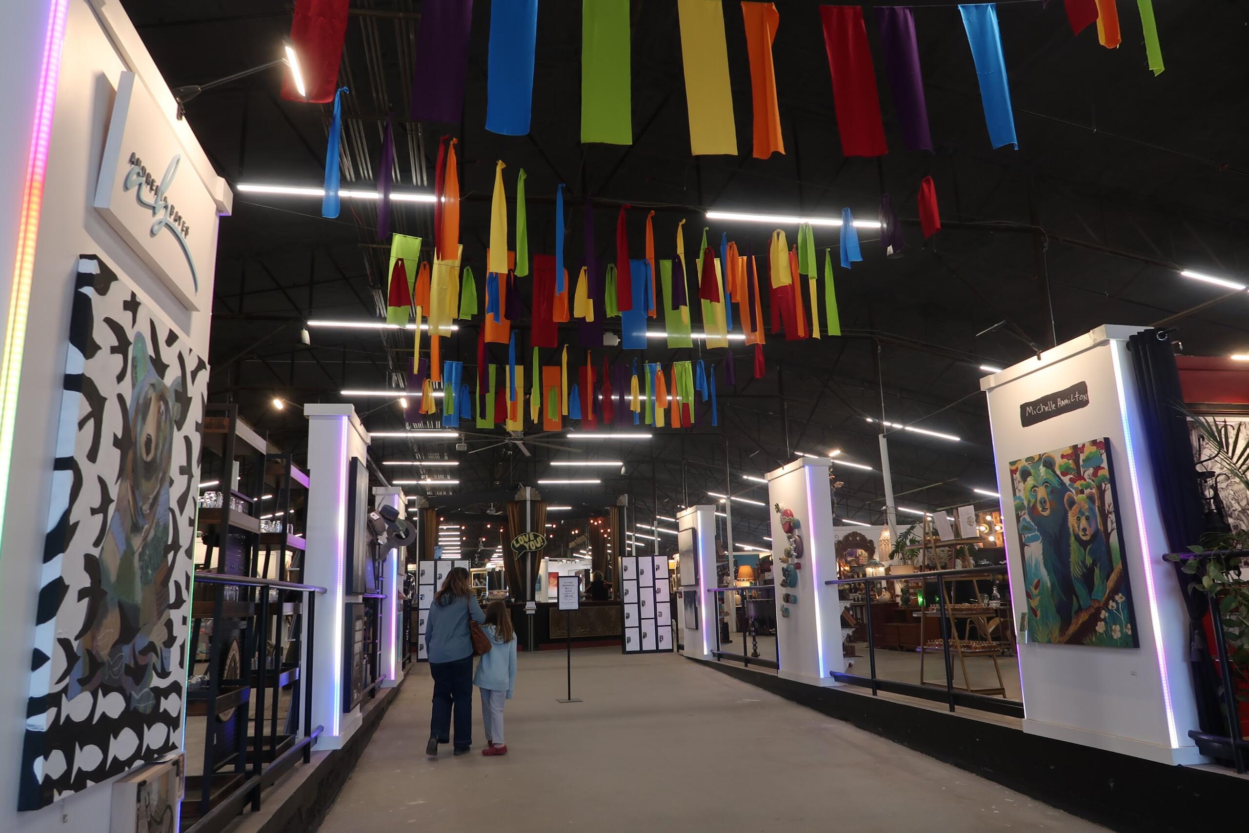 Indoor exhibition hall with booths and multicolored fabric ribbons hanging from the ceiling overhead.