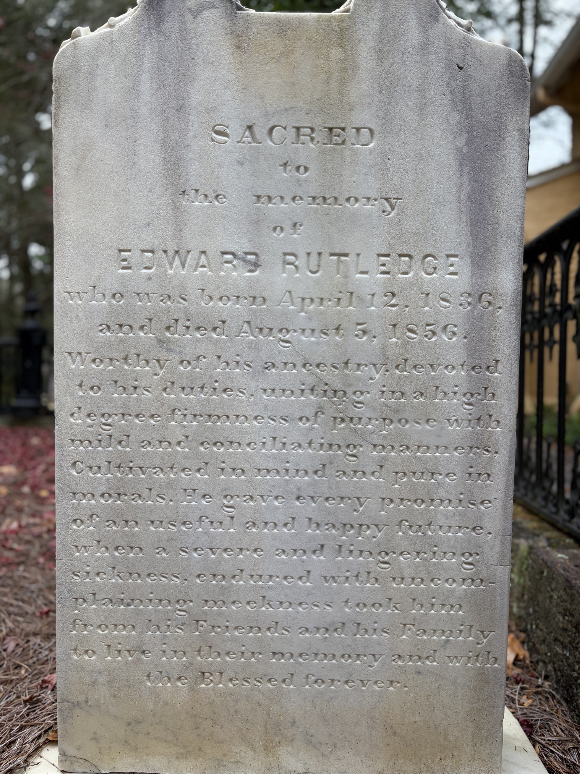 Tall weathered gravestone with carved inscription reading 'Sacred to the memory of Edward Butledge' in a graveyard setting.