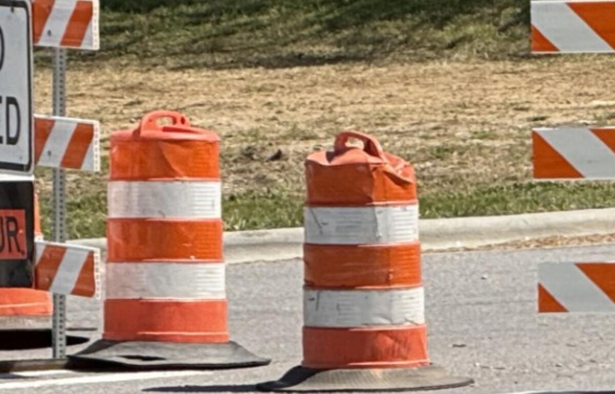 Orange and white striped traffic barrels and barriers marking a road construction zone ahead.