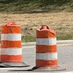 Orange and white striped traffic barrels and barriers marking a road construction zone ahead.