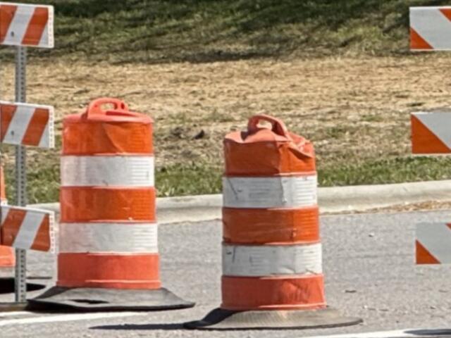 Orange and white striped traffic barrels and barriers marking a road construction zone ahead.