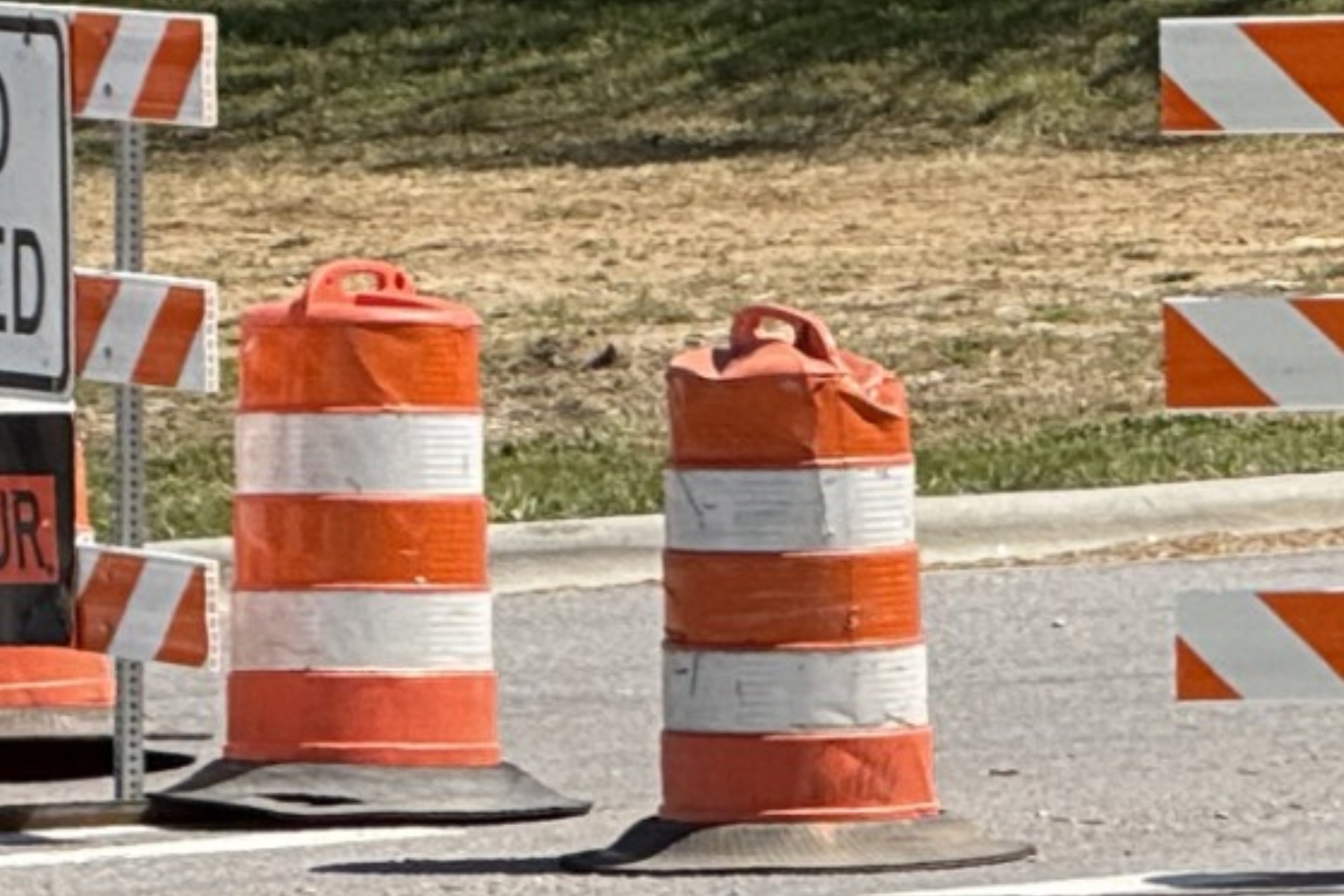 Orange and white striped traffic barrels and barriers marking a road construction zone ahead.