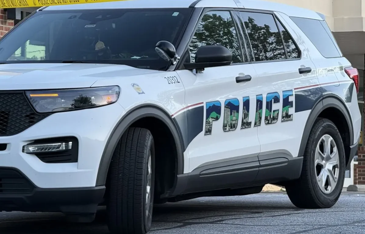 White police SUV parked near a building with yellow police tape across the scene, 'POLICE' lettering visible on the side.