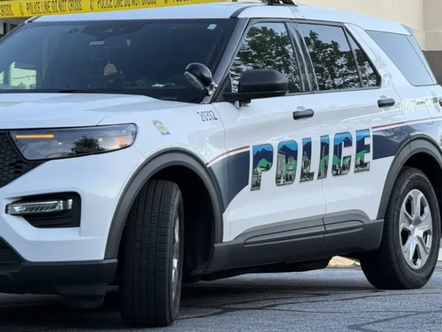 White police SUV parked near a building with yellow police tape across the scene, 'POLICE' lettering visible on the side.