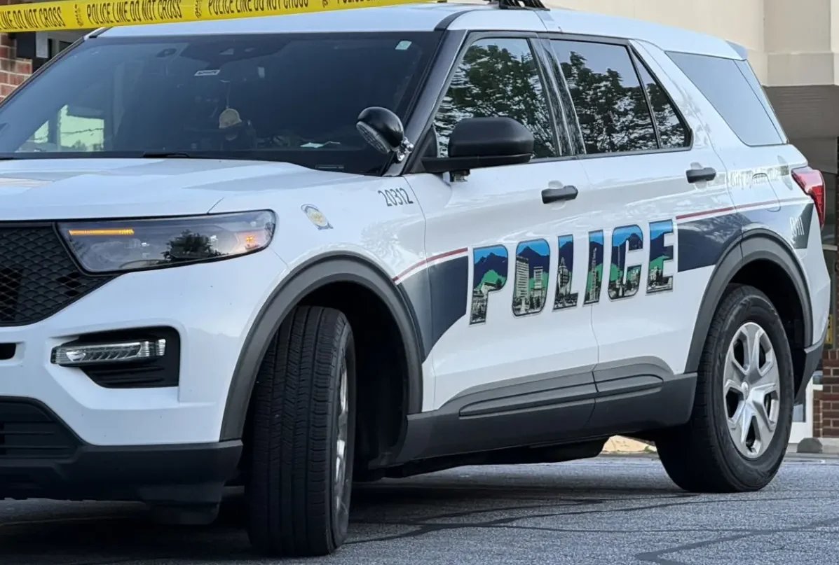 White police SUV parked near a building with yellow police tape across the scene, 'POLICE' lettering visible on the side.