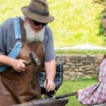 Two older adults outside, man with a beard and hat hammering metal while a woman in a pink vest watches nearby.