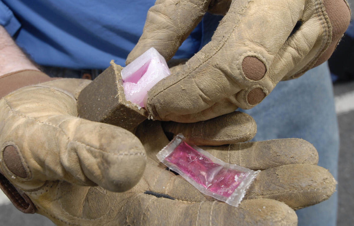 Close-up of dirt-streaked work gloves holding a pink candy wrapped in clear plastic.