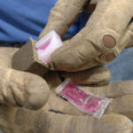 Close-up of dirt-streaked work gloves holding a pink candy wrapped in clear plastic.