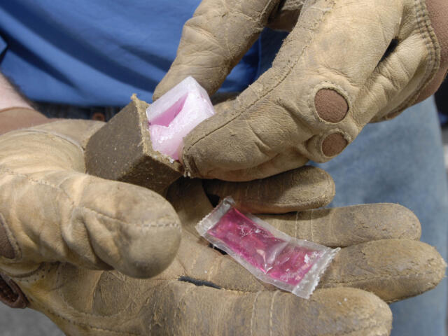 Close-up of dirt-streaked work gloves holding a pink candy wrapped in clear plastic.