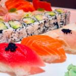 Assorted sushi platter with nigiri (salmon, tuna, white fish) and cucumber–avocado maki rolls, wasabi on the side.