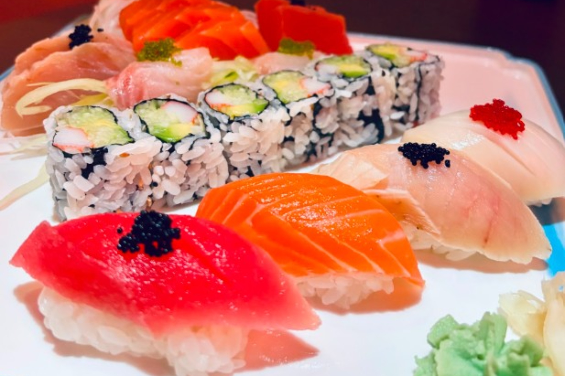 Assorted sushi platter with nigiri (salmon, tuna, white fish) and cucumber–avocado maki rolls, wasabi on the side.