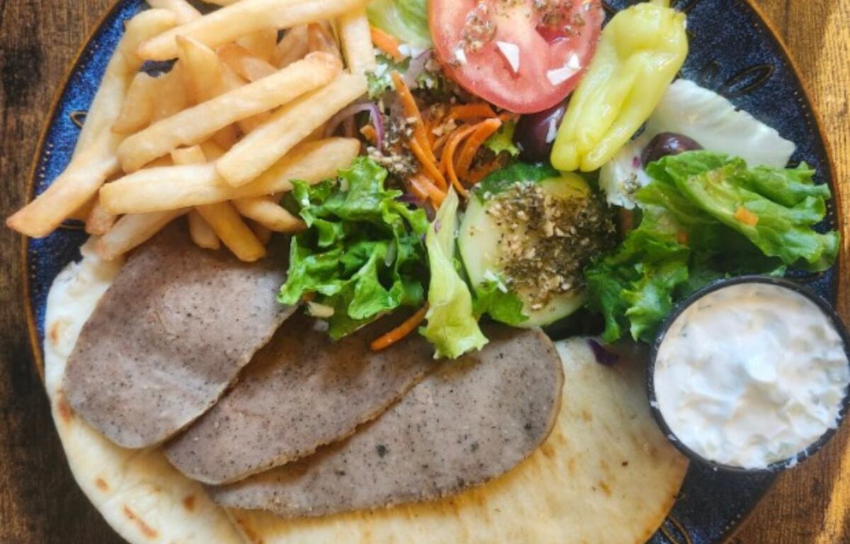 Plate with falafel, pita, and a side of fries plus a fresh salad (lettuce, tomato) and a small cup of yogurt dip.