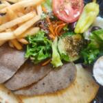 Plate with falafel, pita, and a side of fries plus a fresh salad (lettuce, tomato) and a small cup of yogurt dip.