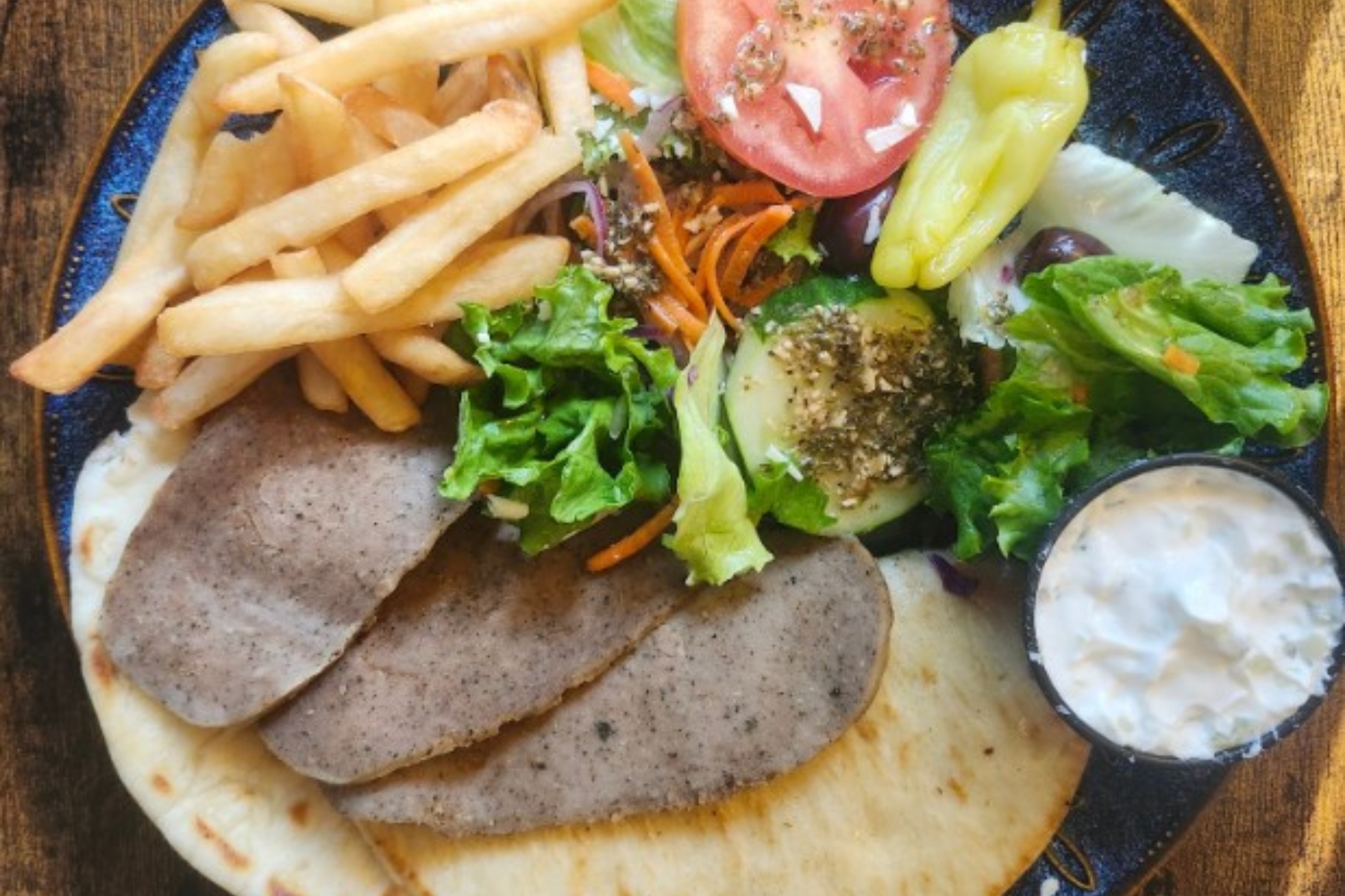 Plate with falafel, pita, and a side of fries plus a fresh salad (lettuce, tomato) and a small cup of yogurt dip.