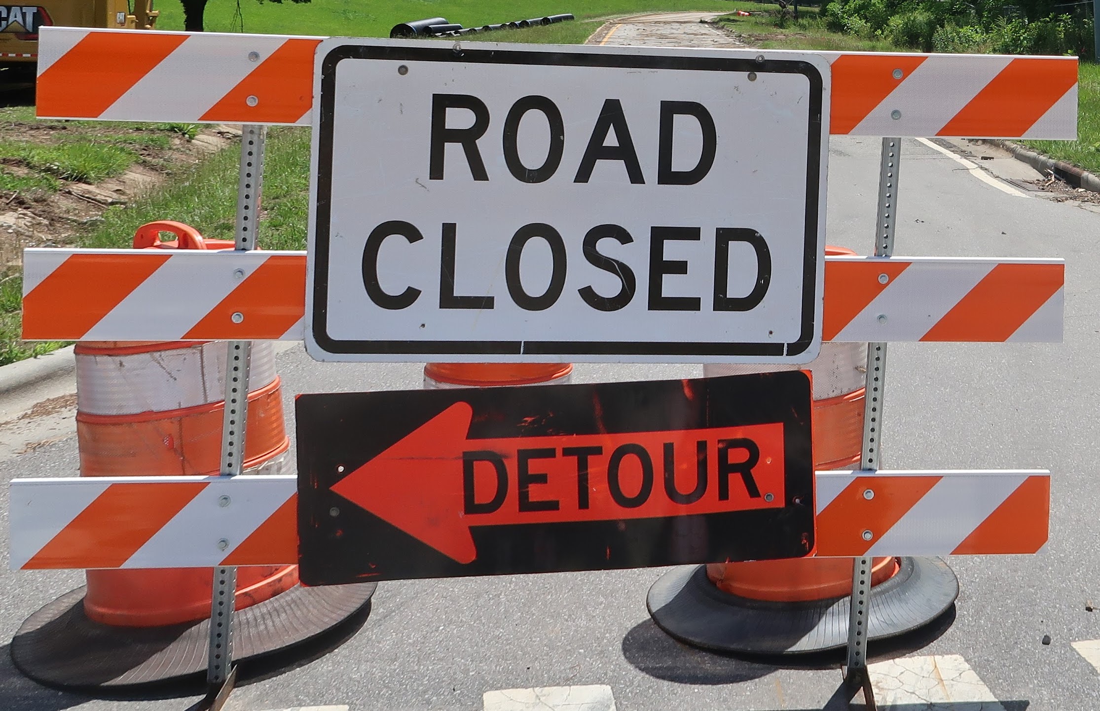 Road closed barrier with orange-and-white striped barricades and a detour sign blocking the road, directing traffic away from the closed area.