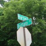 Intersection street signs reading Burton St and Buffalo St, set against dense green foliage.