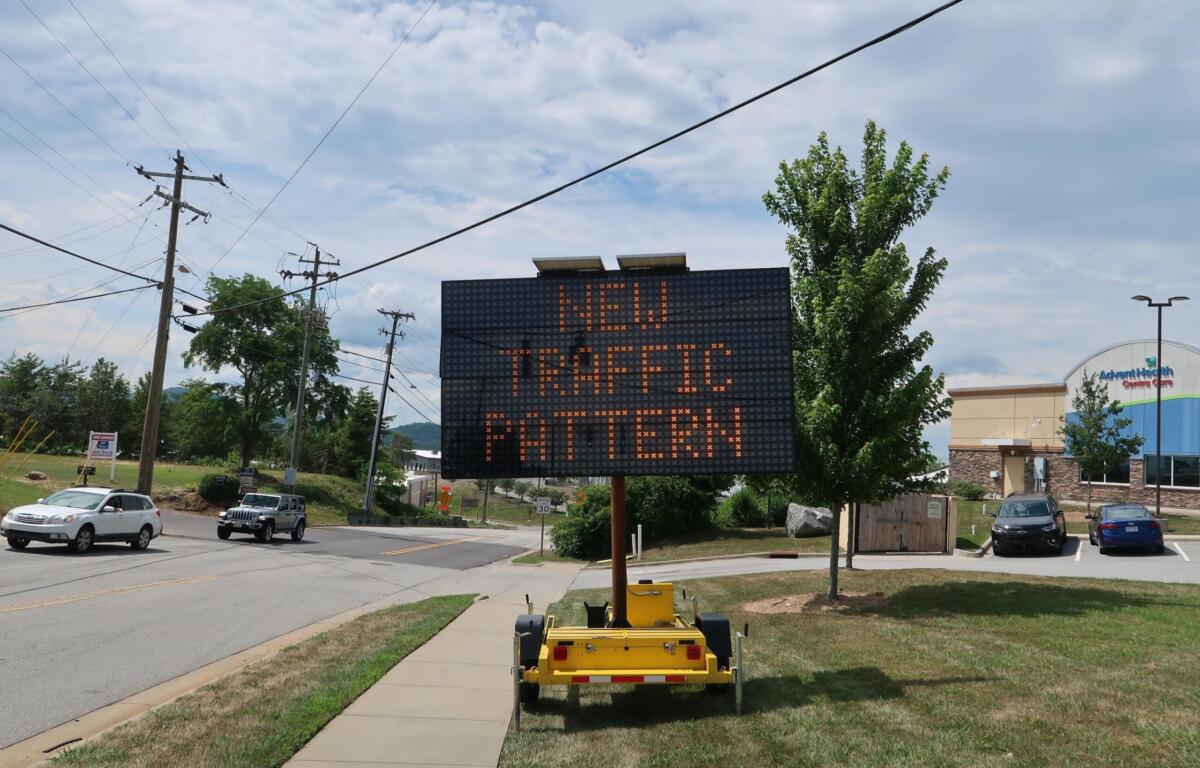 Mobile LED traffic sign on a trailer displaying a message about new traffic; utility poles and a sunny street in the background.