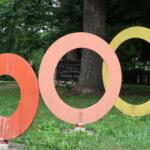 Colorful overlapping circular rings sculpture in a green park with trees in the background.