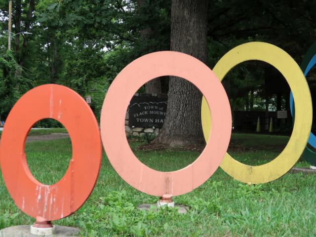 Colorful overlapping circular rings sculpture in a green park with trees in the background.