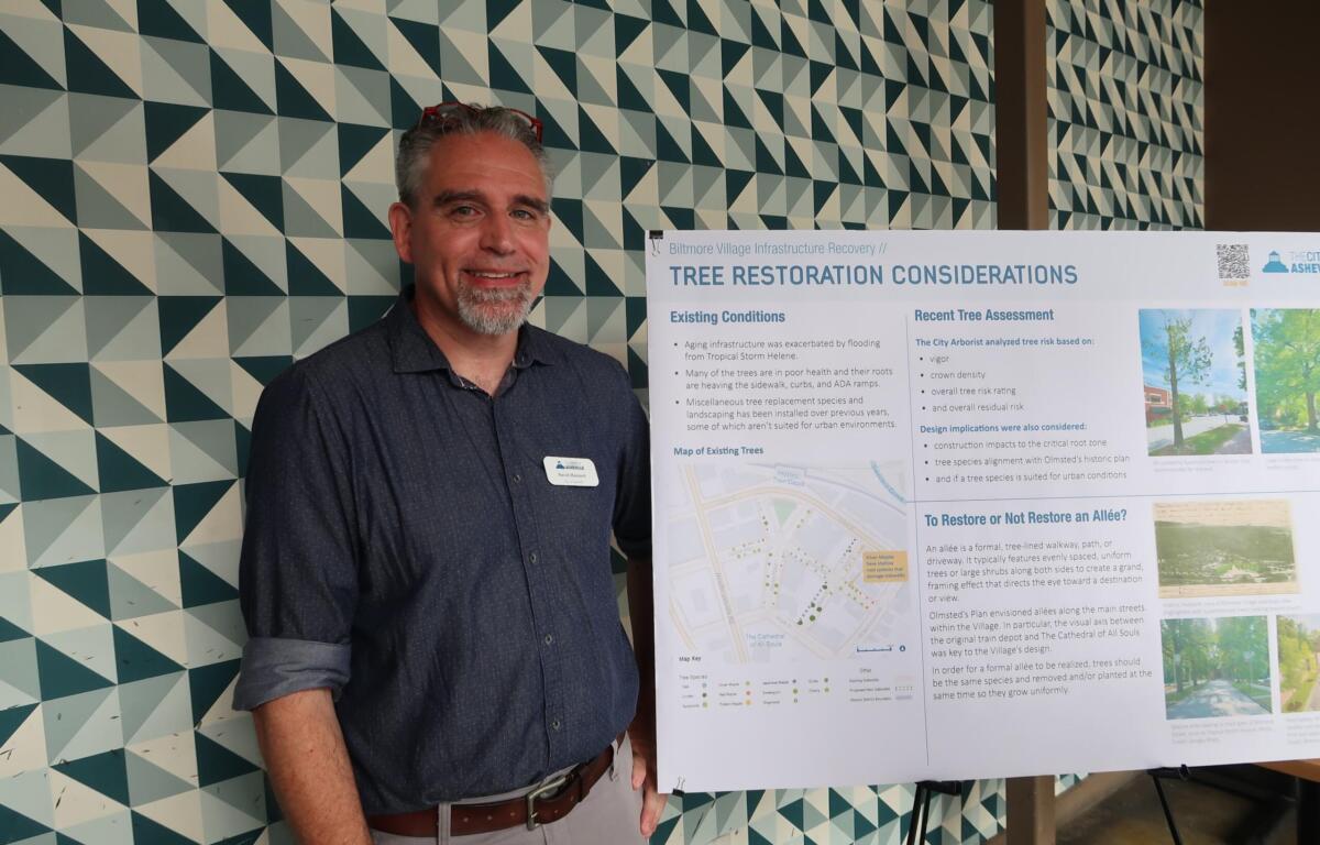 Man standing beside an informational poster on 'Tree Restoration Considerations,' indoors, patterned geometric wall in background.