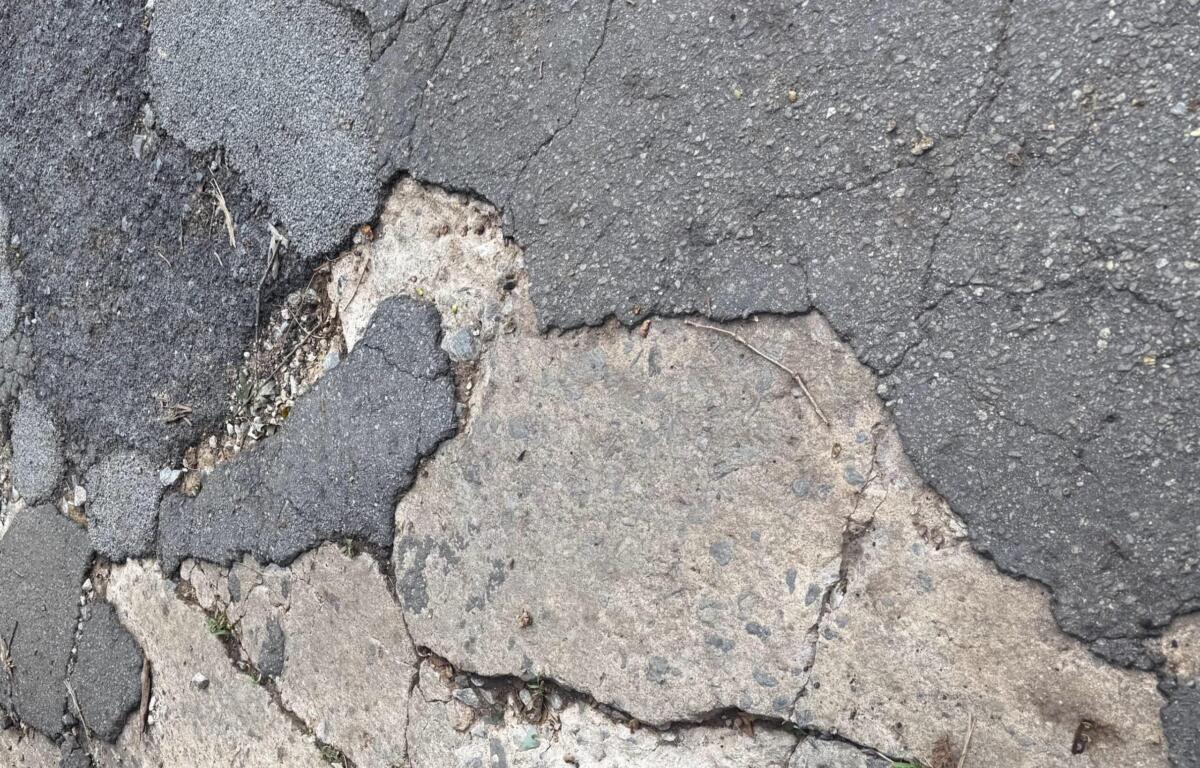 Cracked asphalt road with exposed layers and loose gravel nearby
