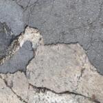 Cracked asphalt road with exposed layers and loose gravel nearby