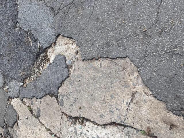 Cracked asphalt road with exposed layers and loose gravel nearby