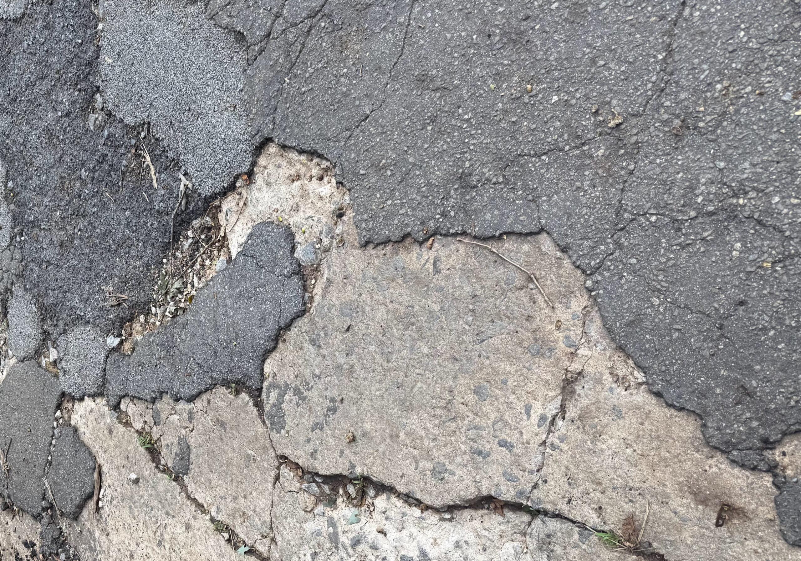 Cracked asphalt road with exposed layers and loose gravel nearby