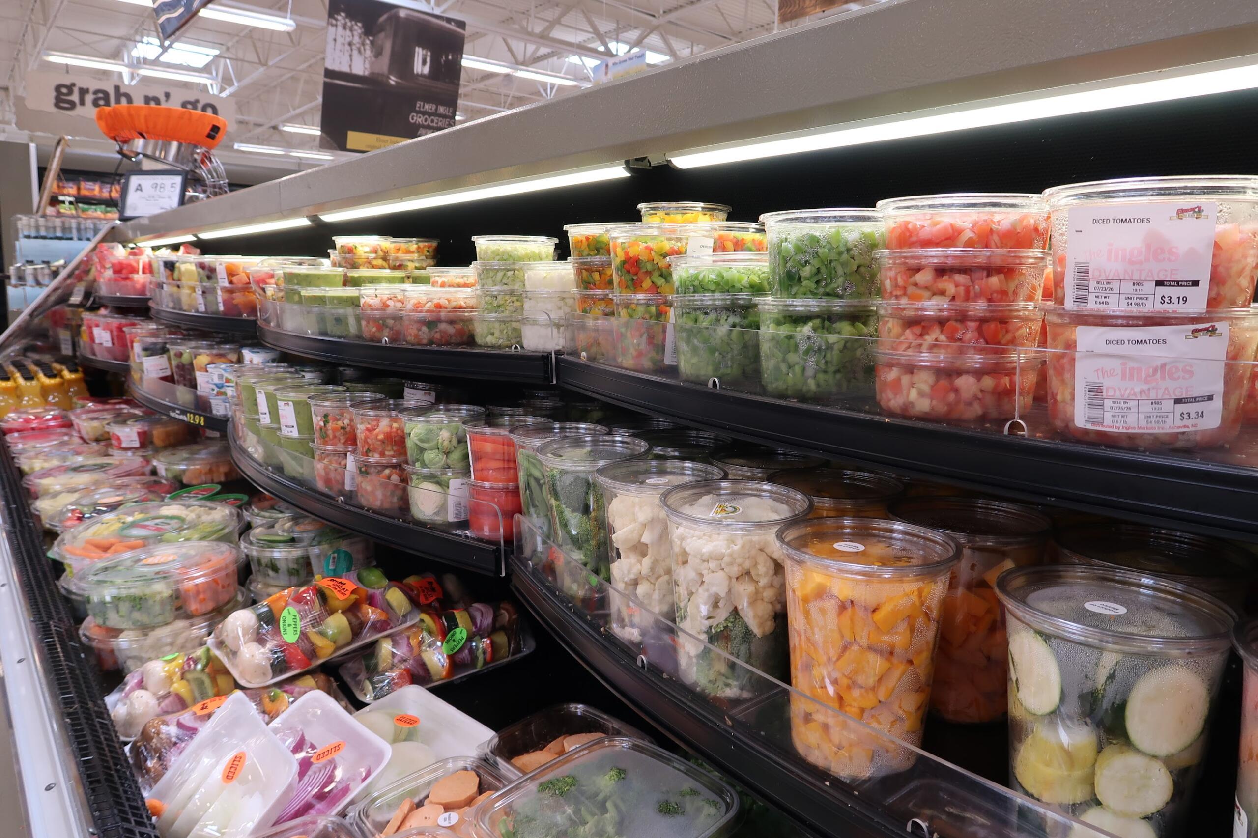 Curved refrigerated display of clear containers filled with colorful diced vegetables and fruits at a supermarket salad bar area
