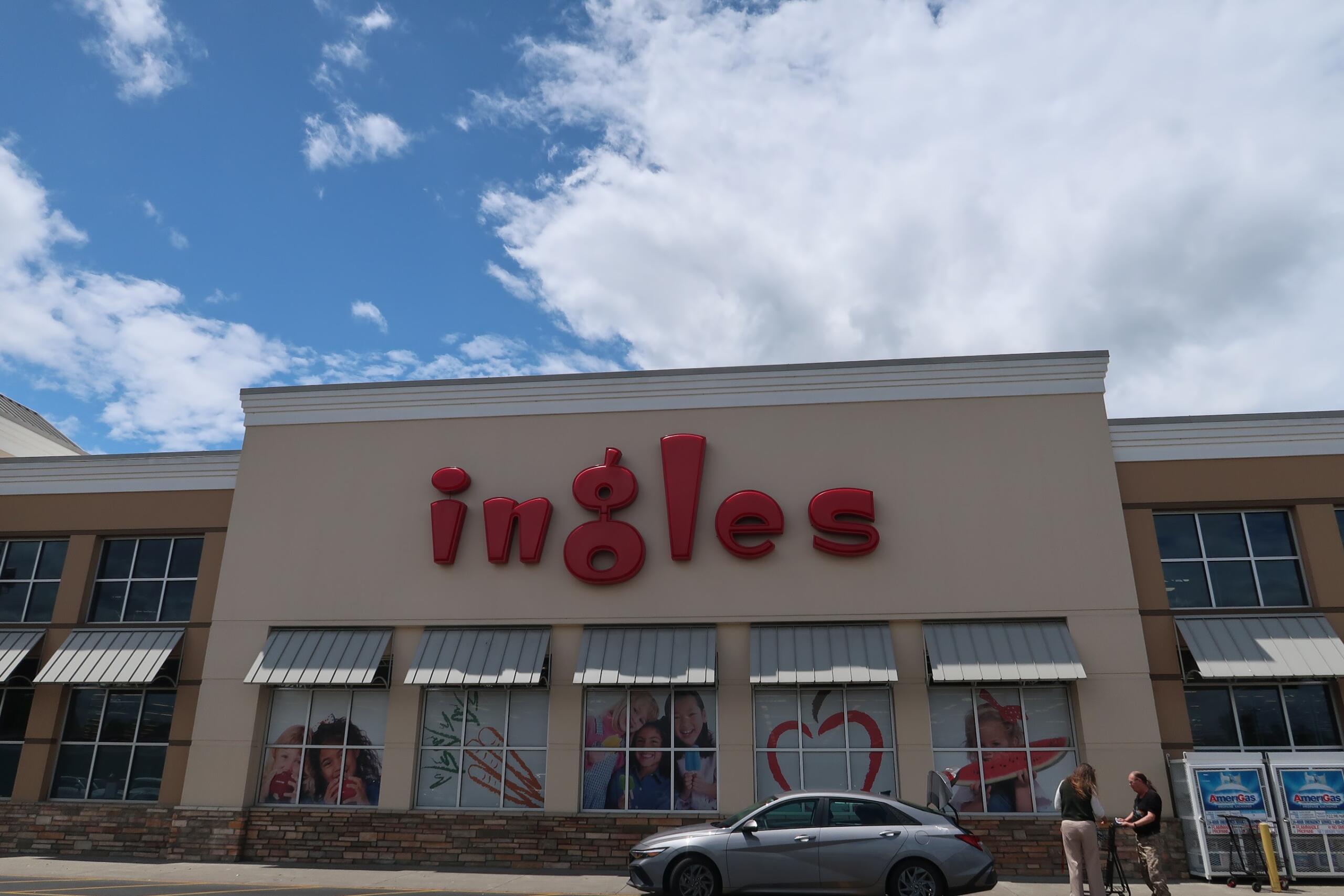 Facade of a shopping center with large red letters on a beige wall; windows show photos and posters under a bright blue sky.