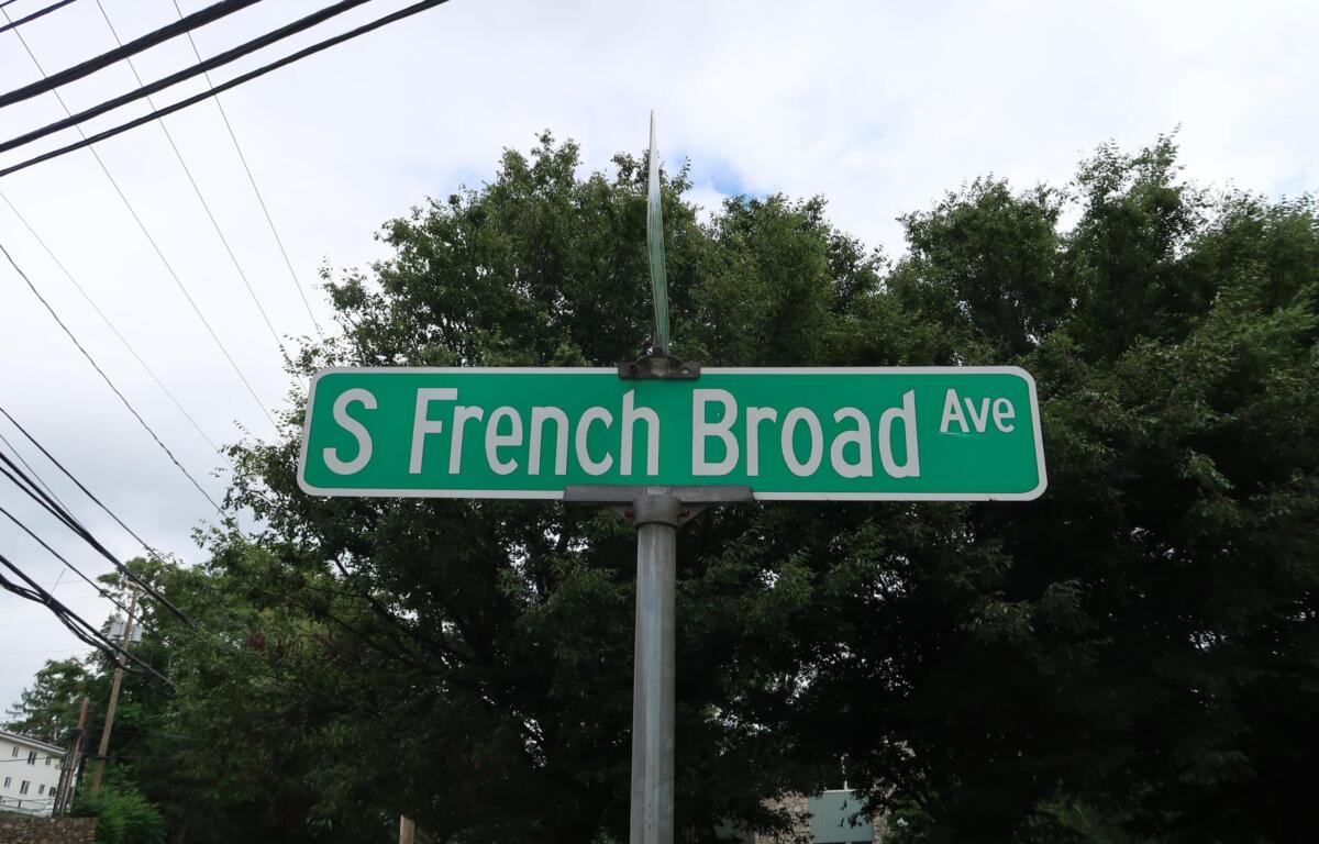 Green street sign reading "S French Broad Ave" with trees and power lines in the background.